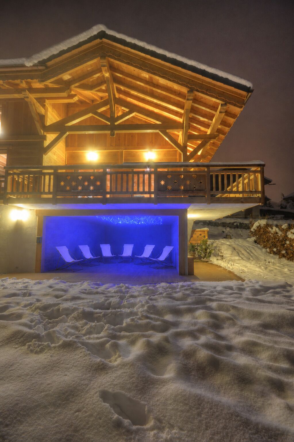 A wooden chalet with a covered outdoor area and a blue-lit pool.