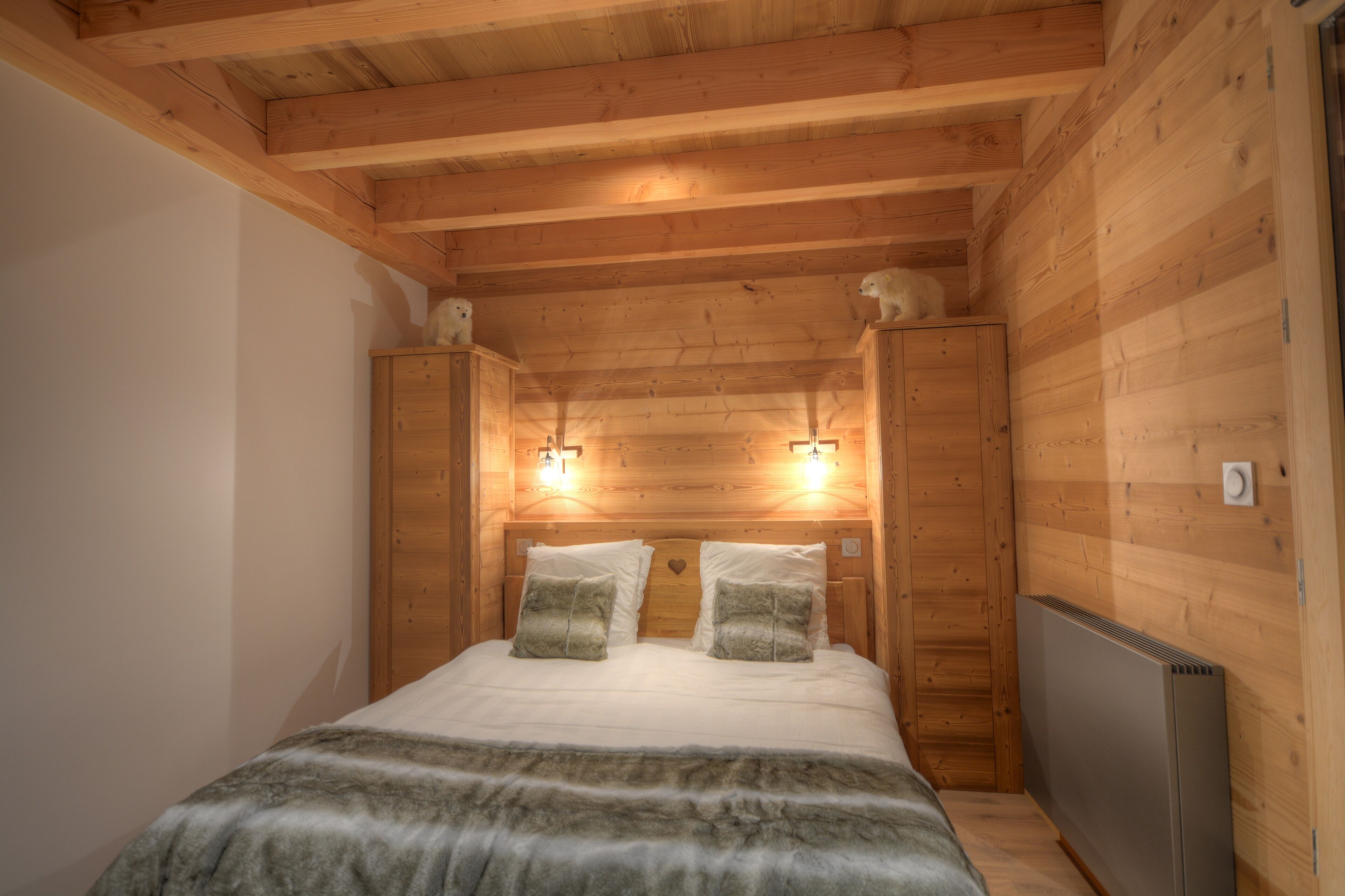 Een houten slaapkamer met een bed, twee wandlampen en een radiator.