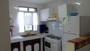 A kitchen with white cabinets, a gas stove, a refrigerator, and a window with curtains.