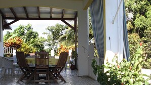 An outdoor patio with a tiled floor, a covered table with chairs, and surrounding greenery.