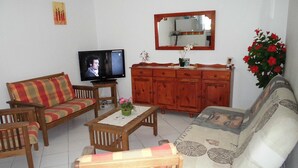 A living room with a sofa, armchairs, a coffee table, a television, a wooden cabinet, and a mirror.
