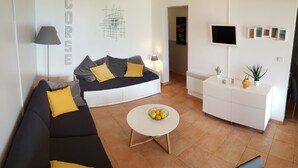 A modern living room with a sofa, a coffee table with fruit, a white cabinet, and a TV on the wall. - Resa 2025 open! SUPERB SEA VIEW mini villa heated pool Serra di Ferro (Serra-Di-Ferro)