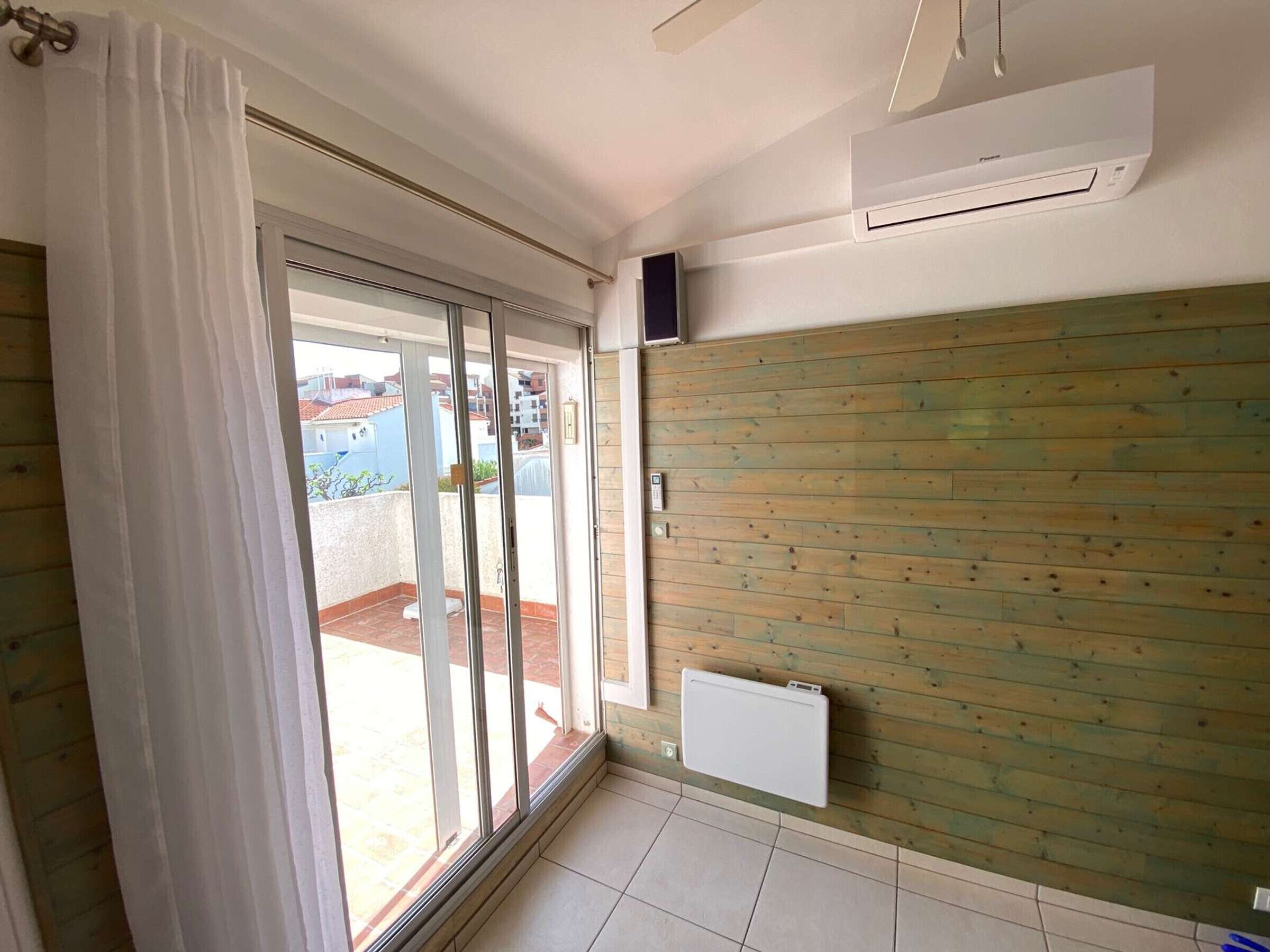 A room with a sliding glass door leading to a balcony, a white radiator, and a ceiling fan.