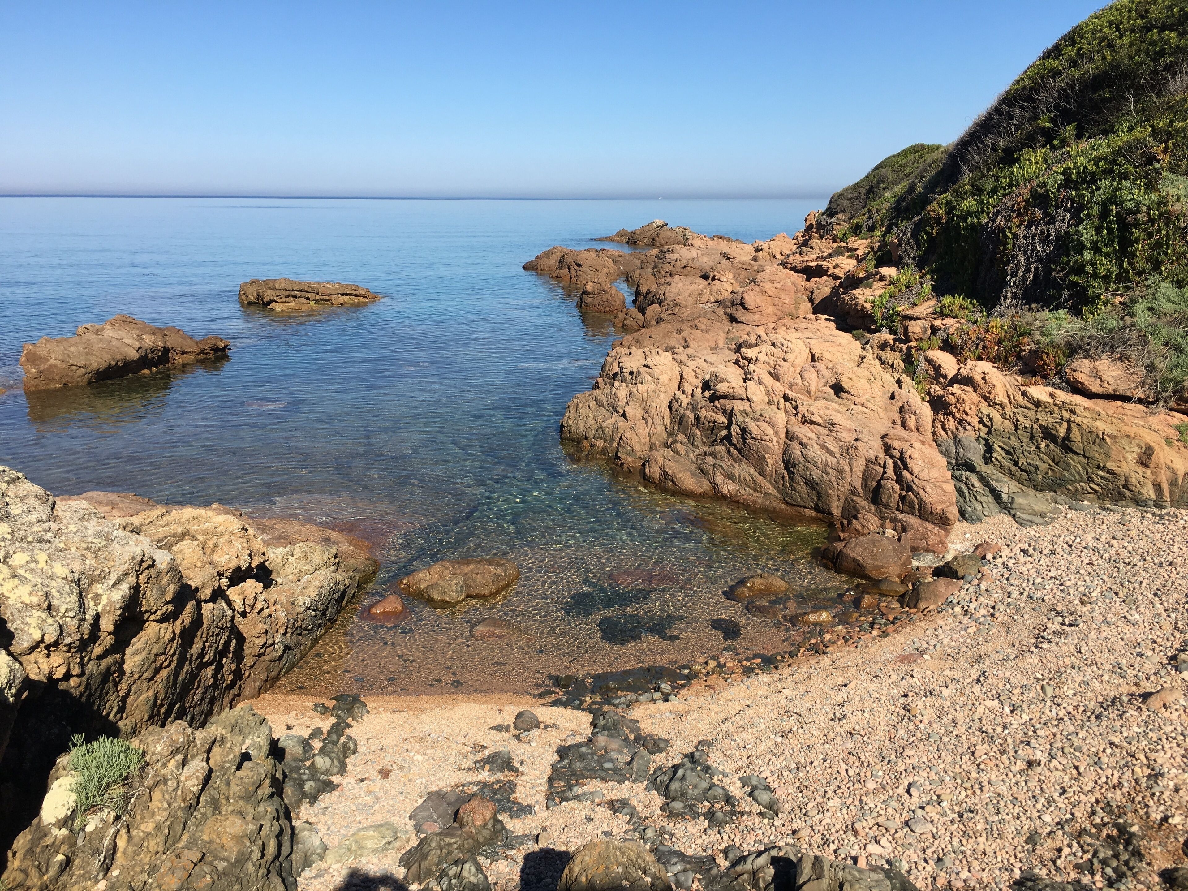 A rocky shoreline with clear water and a distant view of the sea.