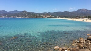 Paesaggio costiero con acque turchesi cristalline, un litorale roccioso e una catena montuosa in lontananza.