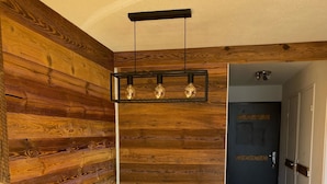 A wooden interior with a dining table, a hanging light fixture, and a door in the background.