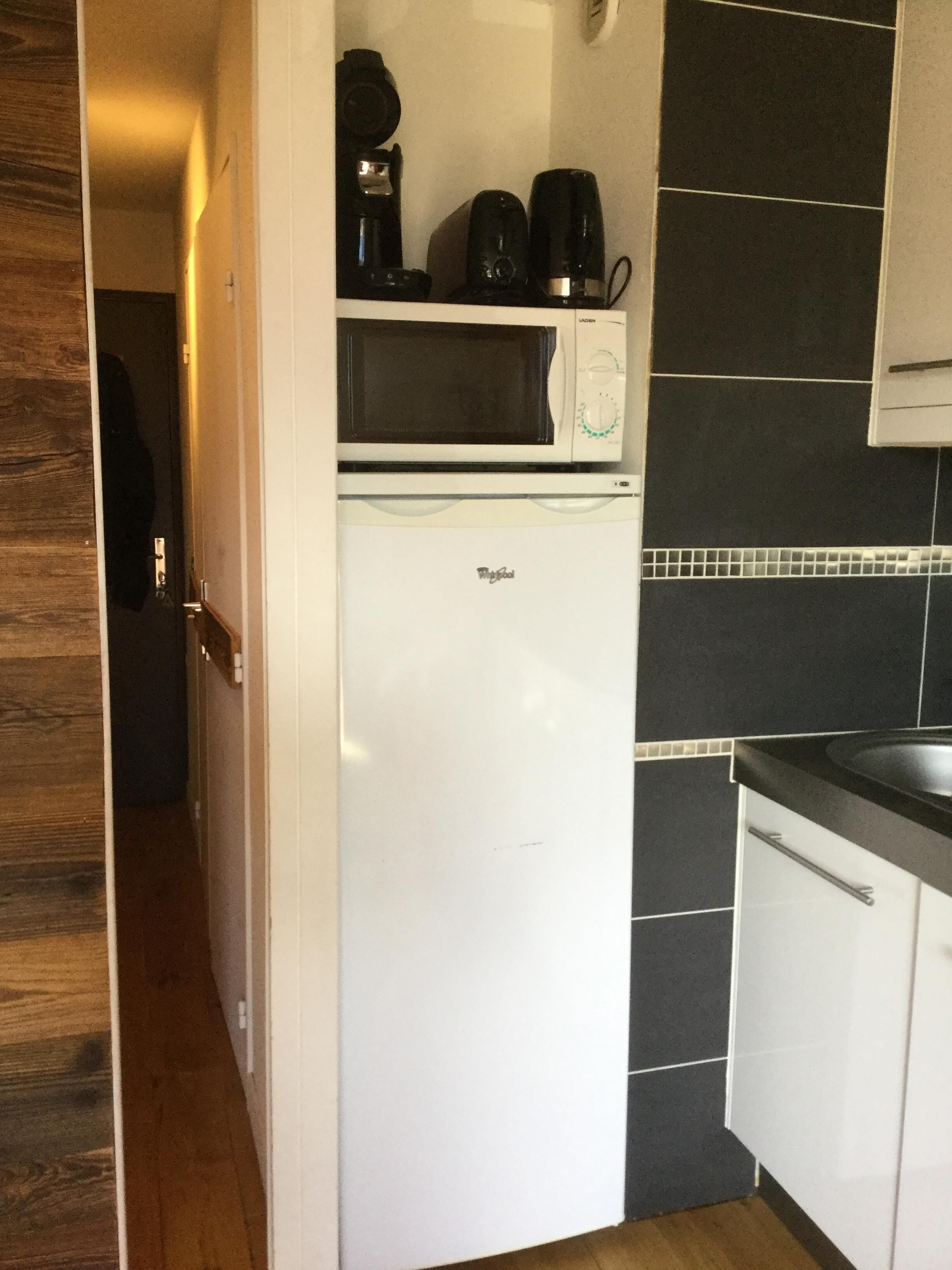 A compact kitchen with a white refrigerator, a microwave, and a coffee maker on top.