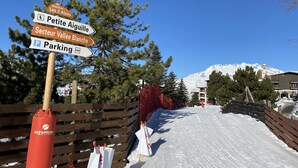 A snowy path with directional signs, a wooden fence, and a mountain in the background.