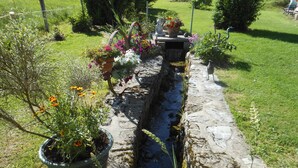 A stone water channel with potted plants and flowers, surrounded by a grassy landscape and a fence. - rental in the countryside in a quiet location   (Foncine-Le-Haut)