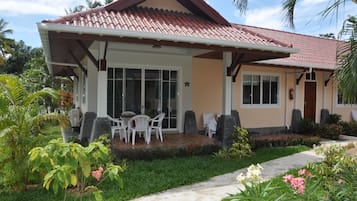 A two-story house with a tiled roof, a covered patio with outdoor furniture, and a well-maintained garden.