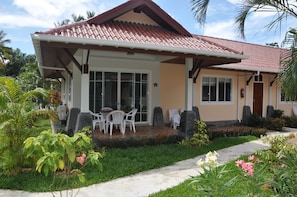 A two-story house with a tiled roof, a covered patio with outdoor furniture, and a well-maintained garden.