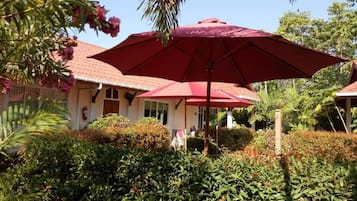 A building with a red umbrella, surrounded by lush greenery and a clear blue sky.