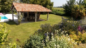 Un espacio de estar al aire libre cubierto, con piscina y jardín lleno de plantas y flores.