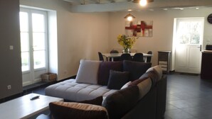 Una sala de estar moderna con un sofá, una mesa de comedor y sillas. Hay una ventana que proporciona luz natural y una puerta que da al exterior.