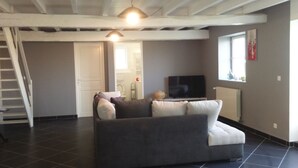 Una sala de estar con un sofá gris, un televisor y una ventana.