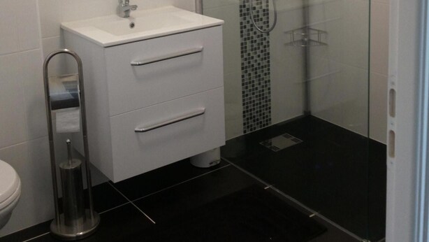 Un baño moderno con un tocador blanco, cabina de ducha de vidrio y piso cubierto de baldosas negras.