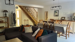 A modern living room with a sectional sofa, a wooden dining table, and a staircase. - Cute house with pool in picturesque village of the Massif des Maures (Collobrières)
