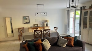 A living room with a dark sofa, a wooden dining table, and a large mirror on the wall. - Cute house with pool in picturesque village of the Massif des Maures (Collobrières)
