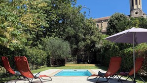 A backyard with a swimming pool, red lounge chairs, and a stone fire pit. - Cute house with pool in picturesque village of the Massif des Maures (Collobrières)