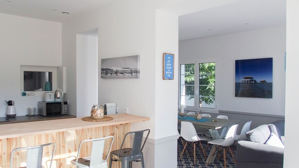 Cozinha moderna com área de bar, espaço de refeições com cadeiras e vista para o oceano através de amplas janelas.