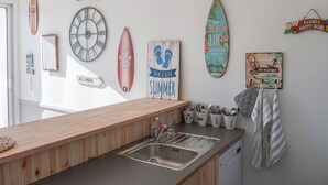 Cozinha com bancada de madeira, pia de aço inoxidável e diversos objetos decorativos de surf e placas na parede.
