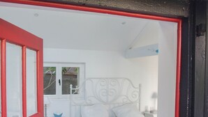 Quarto com uma cama branca, uma mesa de cabeceira e uma porta vermelha.