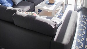 Uma sala de estar moderna com um sofá cinzento, uma mesa de centro e vista para um jardim através de uma porta de vidro.