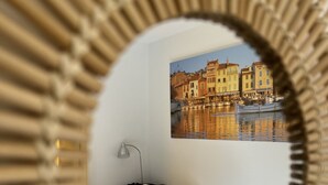 A bedroom with a bed, pillows, a nightstand, a lamp, and a wall-mounted picture of a waterfront scene.