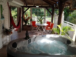 Un jacuzzi en un área exterior cubierta, con una mesa y sillas, rodeado de plantas en macetas y vistas a la vegetación.