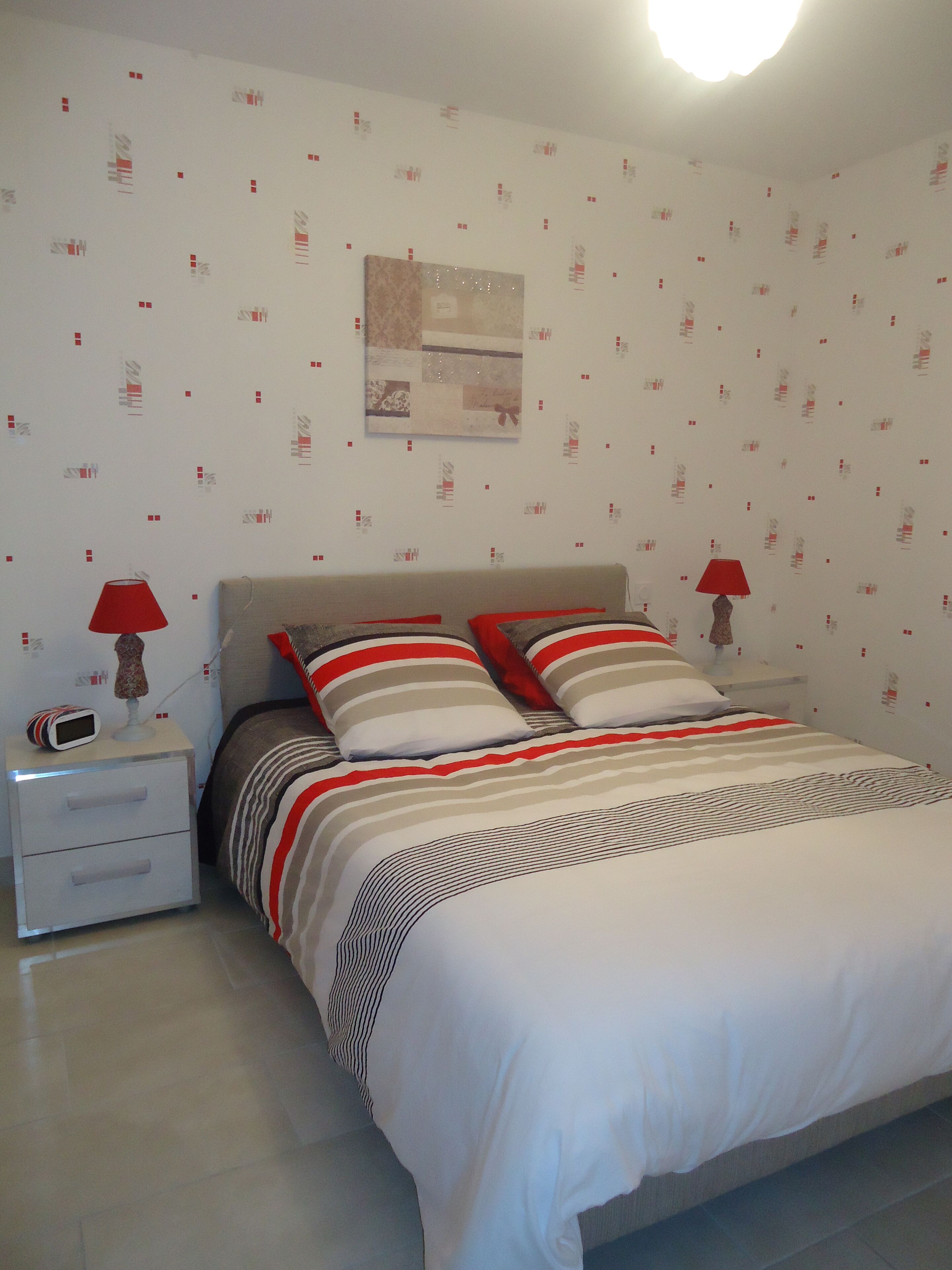 Een slaapkamer met een bed, twee nachtkastjes, een rode lamp op elk en een muur met behang met een patroon.