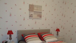 Un dormitorio con una cama, dos mesitas de noche, una lámpara roja en cada una y una pared con papel tapiz estampado.
