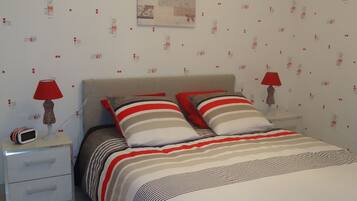 Een slaapkamer met een bed, twee nachtkastjes, een rode lamp op elk en een muur met behang met een patroon.