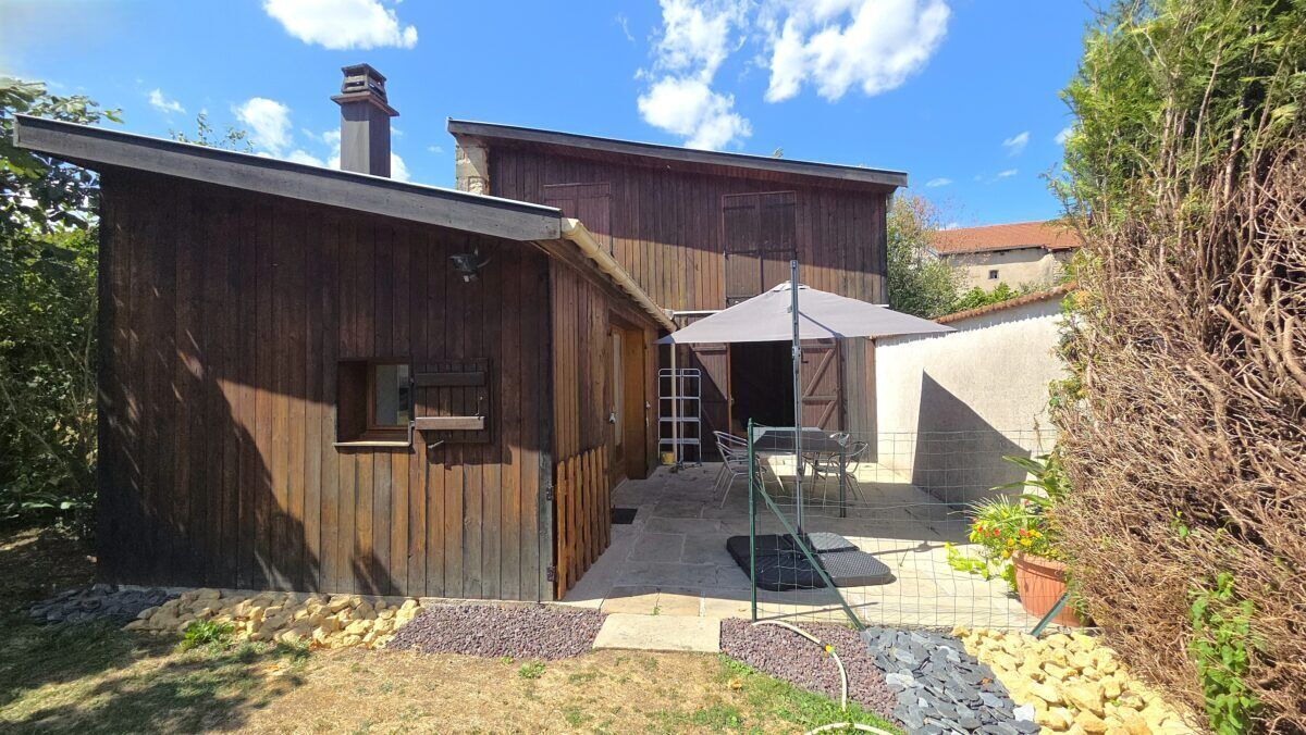A wooden building with a patio area, a covered seating area, and a garden with plants and a small pond.