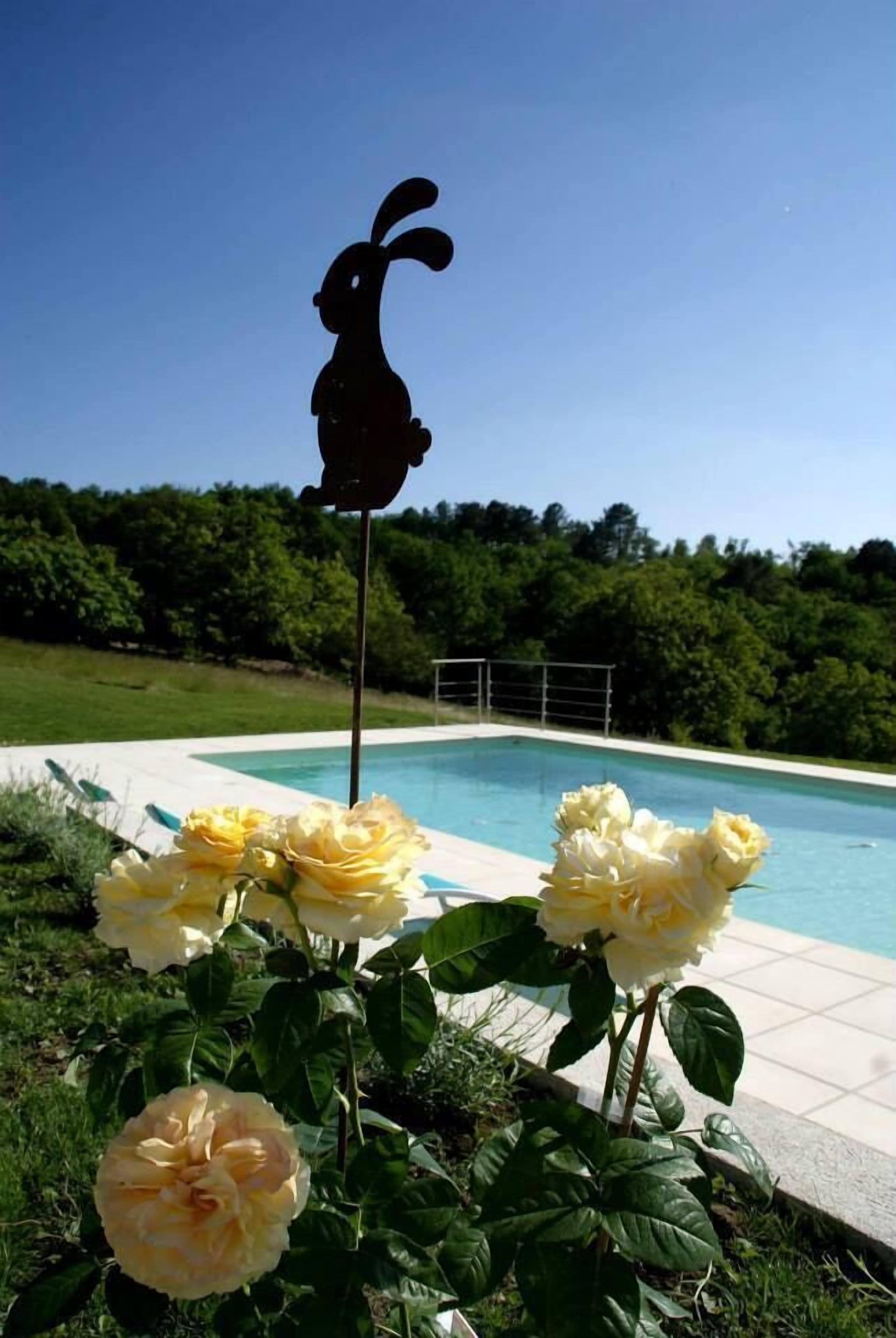 A poolside view with a silhouette of a rabbit decoration, surrounded by yellow roses.