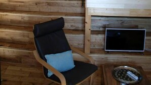 A wooden interior with a sloped ceiling, a chandelier, a black chair with a cushion, and a small table with a tray. - Charming cottage, private turquoise pool, PLAZAC-prox. treasures of Périgord (Plazac)