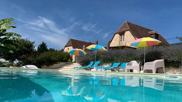 A swimming pool with lounge chairs and umbrellas, surrounded by stone buildings and greenery. - Charming cottage, private turquoise pool, PLAZAC-prox. treasures of Périgord (Plazac)