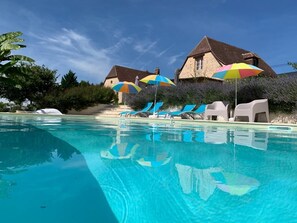 En pool med liggestole og parasoller, omgivet af stengulve og grønt.