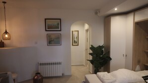 A bedroom with a bed, a radiator, a hanging light fixture, and framed pictures on the wall.