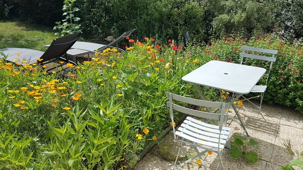 Relax in a serene outdoor space surrounded by vibrant flowers and a low hedge, with a table and two chairs perfect for al fresco dining.