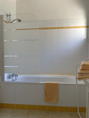 Een badkamer met een bad, een douche en een handdoekrek met handdoeken.