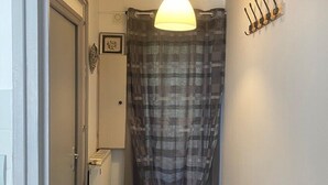 A narrow hallway with a door on the left, a radiator, a patterned rug, a hanging light fixture, and a curtain.