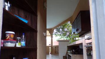 Cocina estrecha con estantes de madera, suelo de baldosas y vista a un árbol.