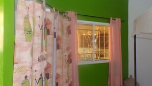 Una habitación con ventana, paredes verdes y una cortina con motivos culturales.