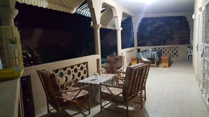 Un área de estar al aire libre techada con una mesa, sillas, una jaula de pájaros y vistas al cielo nocturno.