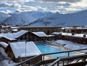 Une station de ski enneigée dotée d’une piscine, de bâtiments en bois et offrant une vue sur les montagnes.