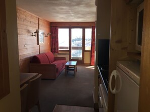 Un espace de vie compact comprenant un canapé, une petite table, un lave-linge et un téléviseur.