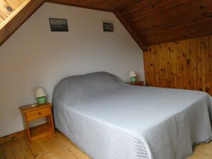 Un dormitorio con una cama individual, piso de madera y techo inclinado.