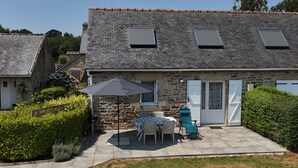 Ein Steinhaus mit Ziegeldach, eine Terrasse mit Tisch und Stühlen sowie ein kleiner Garten.