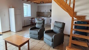Ein geräumiger Wohnbereich mit hoher Decke, einer Holztreppe und einer Küche im Hintergrund.