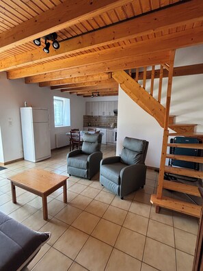 A spacious living area with a high ceiling, a wooden staircase, and a kitchen in the background. - The stable, quiet house in the countryside (Quéménéven)